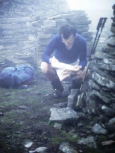 A hiker reads a map by a cairn in the fog in the Lake District