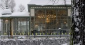 Glass building, snow on roof, chandelier glowing warmly inside.