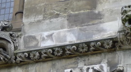 Stone wall with a carved row of flowers and leaves, at each end there is a strange best. One looks like a bat and the other is more like a snarling lion.
