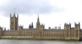 Long brown building with many pointed spires and a giant clock tower at the right hand end, on the far side of a broad river